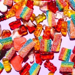 Colorful mix of gummy candies including bears and rainbow strips on a vibrant purple backdrop.